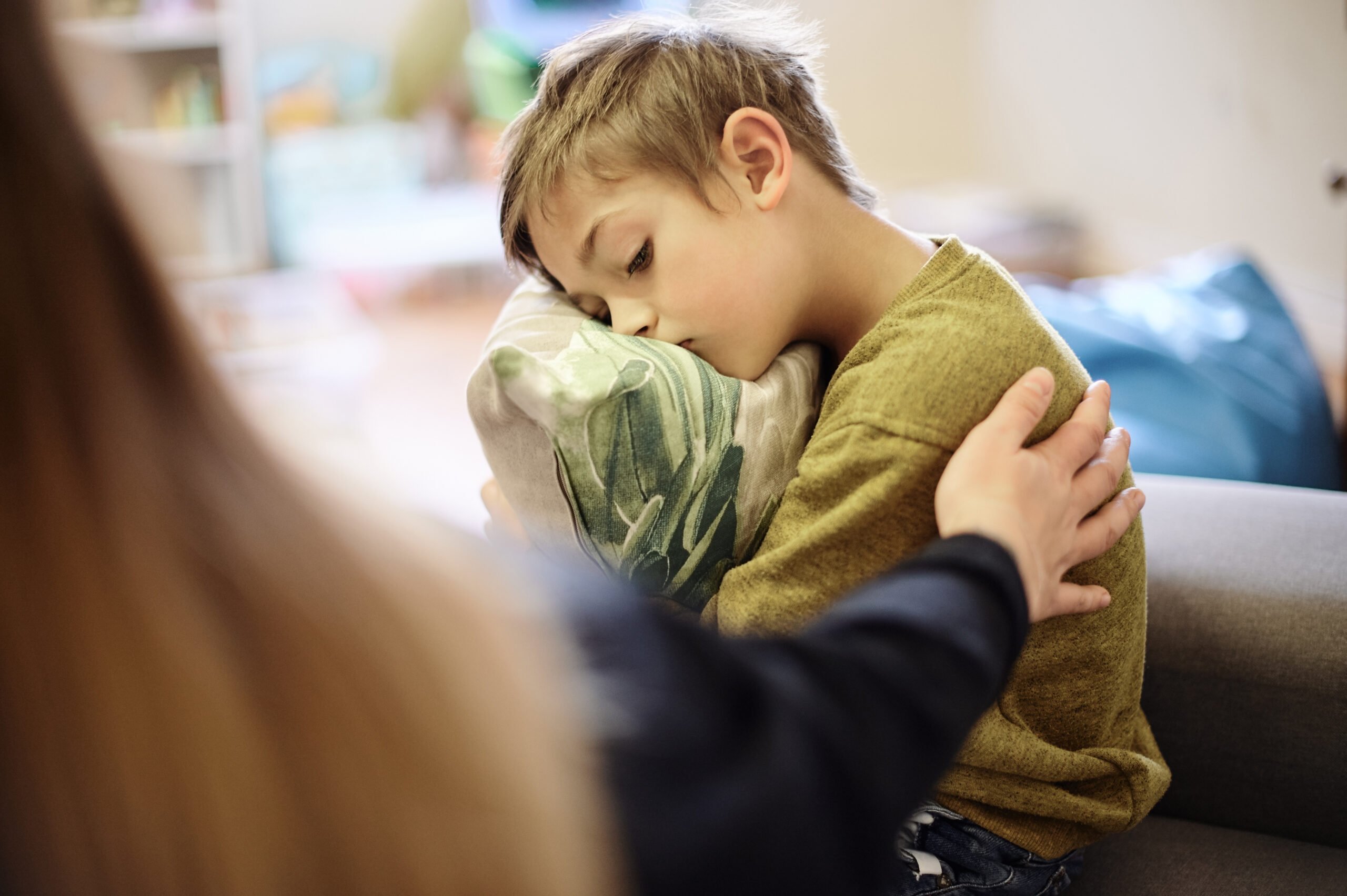 Anxiety, bullying and hand of mother with boy hugging pillow for comfort, compassion and empathy at home. Disability, abuse and mom with sad child suffering depression or mental health problem.