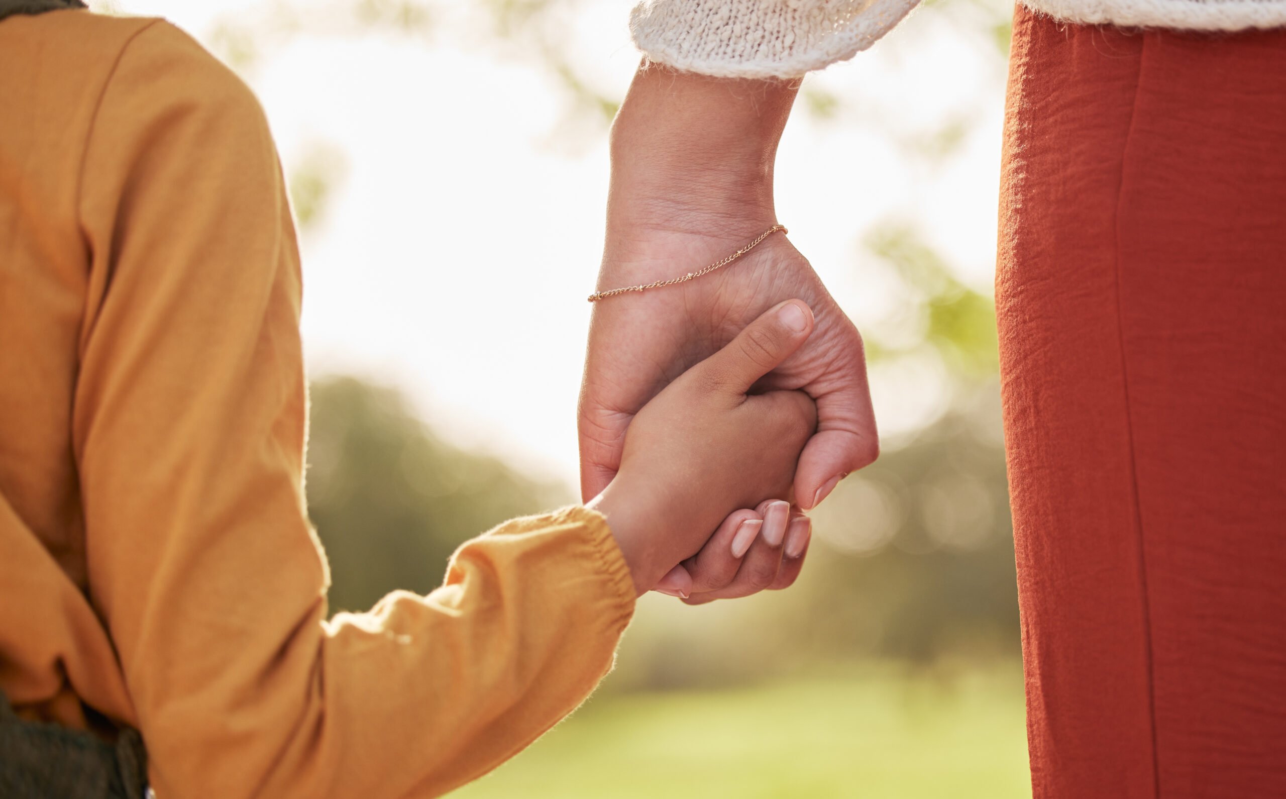 Mother, kid and holding hands for walking in park for support, trust and care together or bonding in nature. Love, comfort and parent help child in the morning sunshine with kindness on weekend.