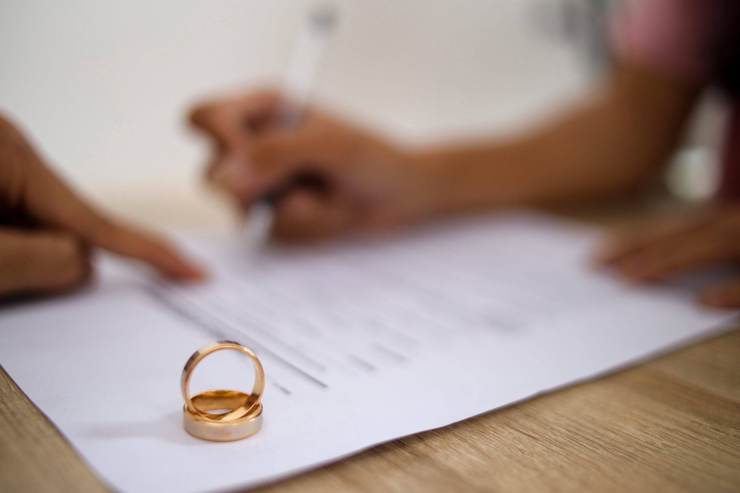 Selective Focus of Wedding Rings Against Woman Hand Filing Divorce Papers or Premarital Agreement Prepared by Lawyer