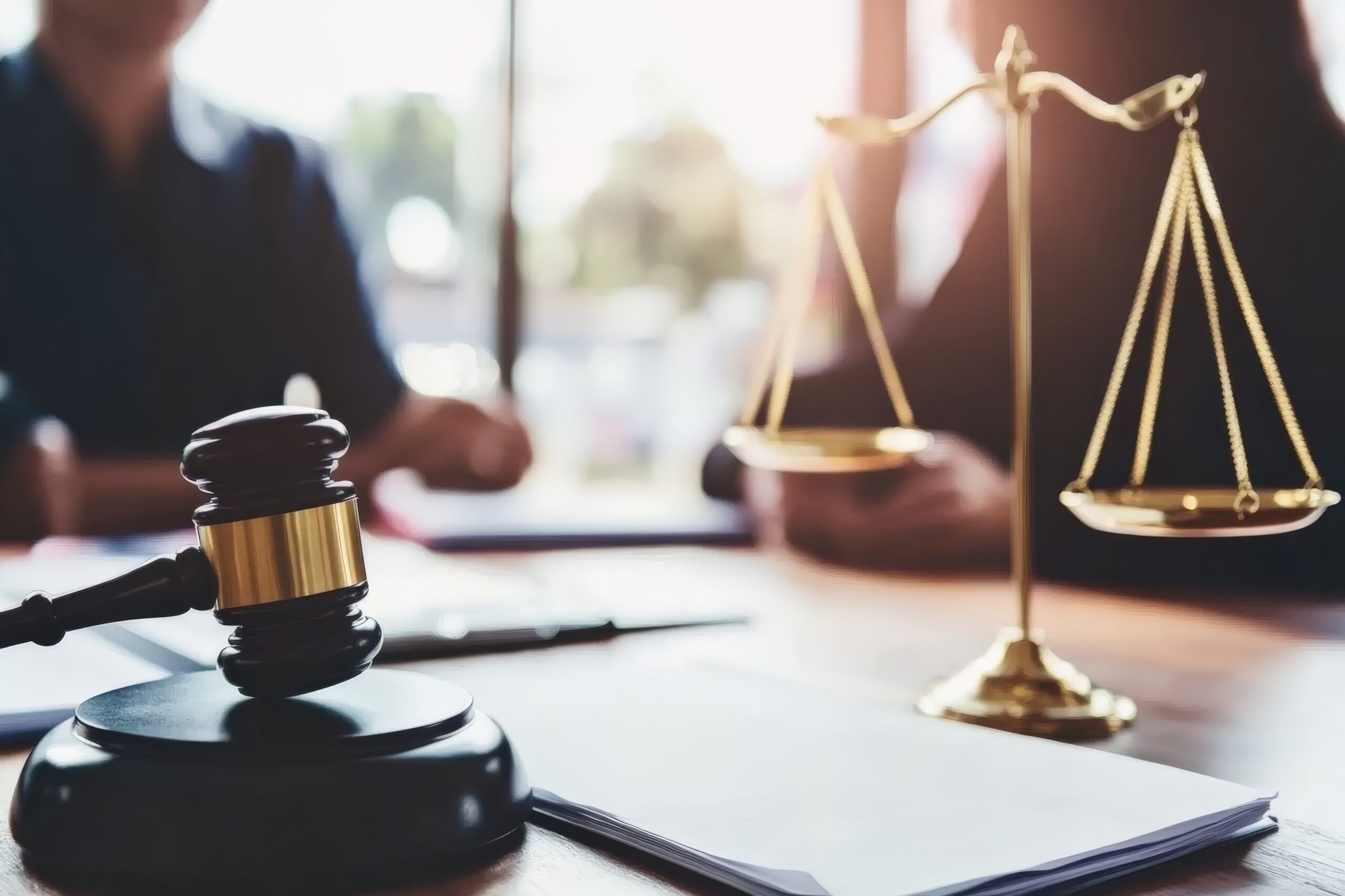 Legal concept featuring a gavel and scales of justice positioned on a lawyer's desk amidst a court hearing environment