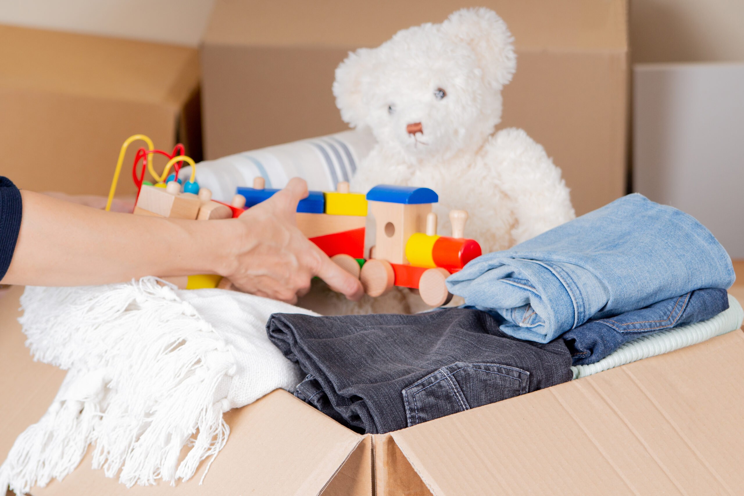 Woman hands collecting donation box with clothes, bed linen, kid toys. Donations for charity, help low income families, declutter, moving moving into new home, recycling, sustainable living.