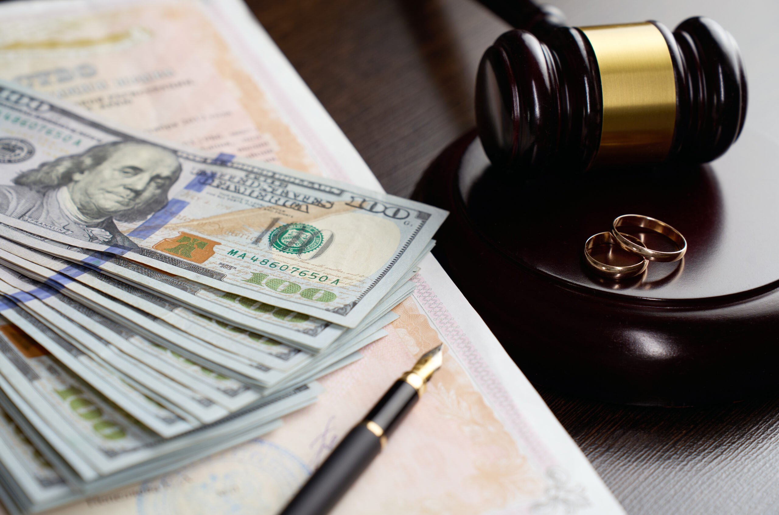 Legal Separation and Alimony Concept. Wedding rings, judge gavel, US dollar bills and blurred marriage certificate. Financial aspects of divorce, including alimony, asset division, and legal expenses