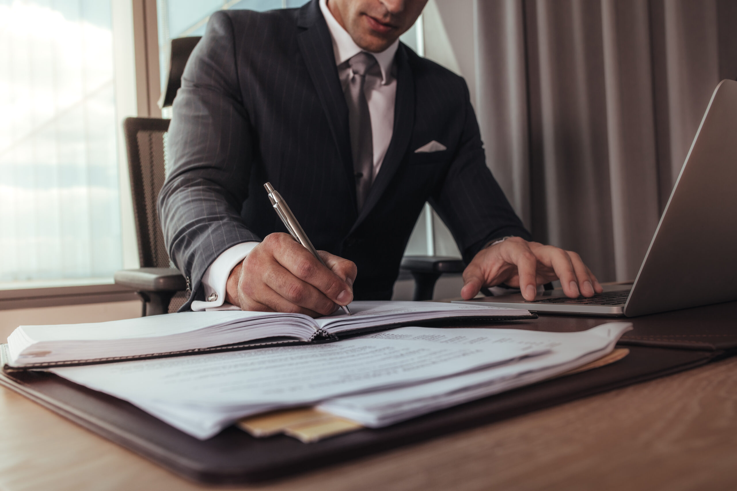 Cropped shot of businessman hands writing in a diary. Man working at his office desk with laptop.