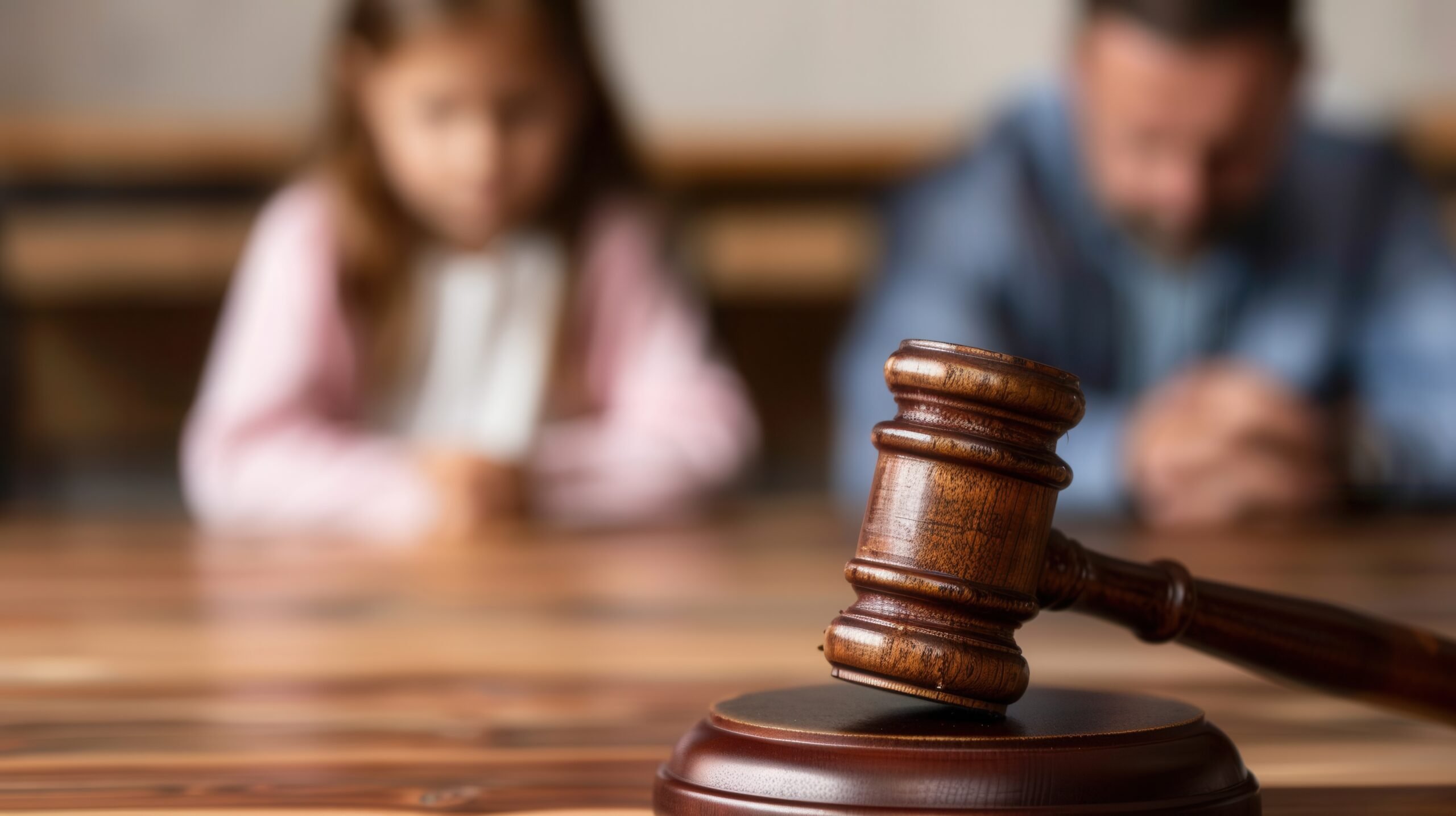 A wooden gavel rests on a wooden sound block, with a blurred child in the background, symbolizing a legal decision about child custody.