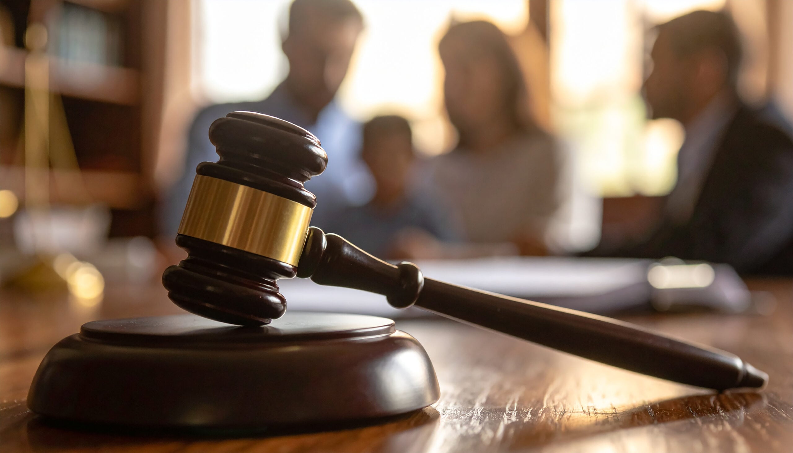 Wooden judge gavel on table, blurred family in courtroom, emotional and dramatic legal dispute scene. Child custody, law and justice. Close-up.