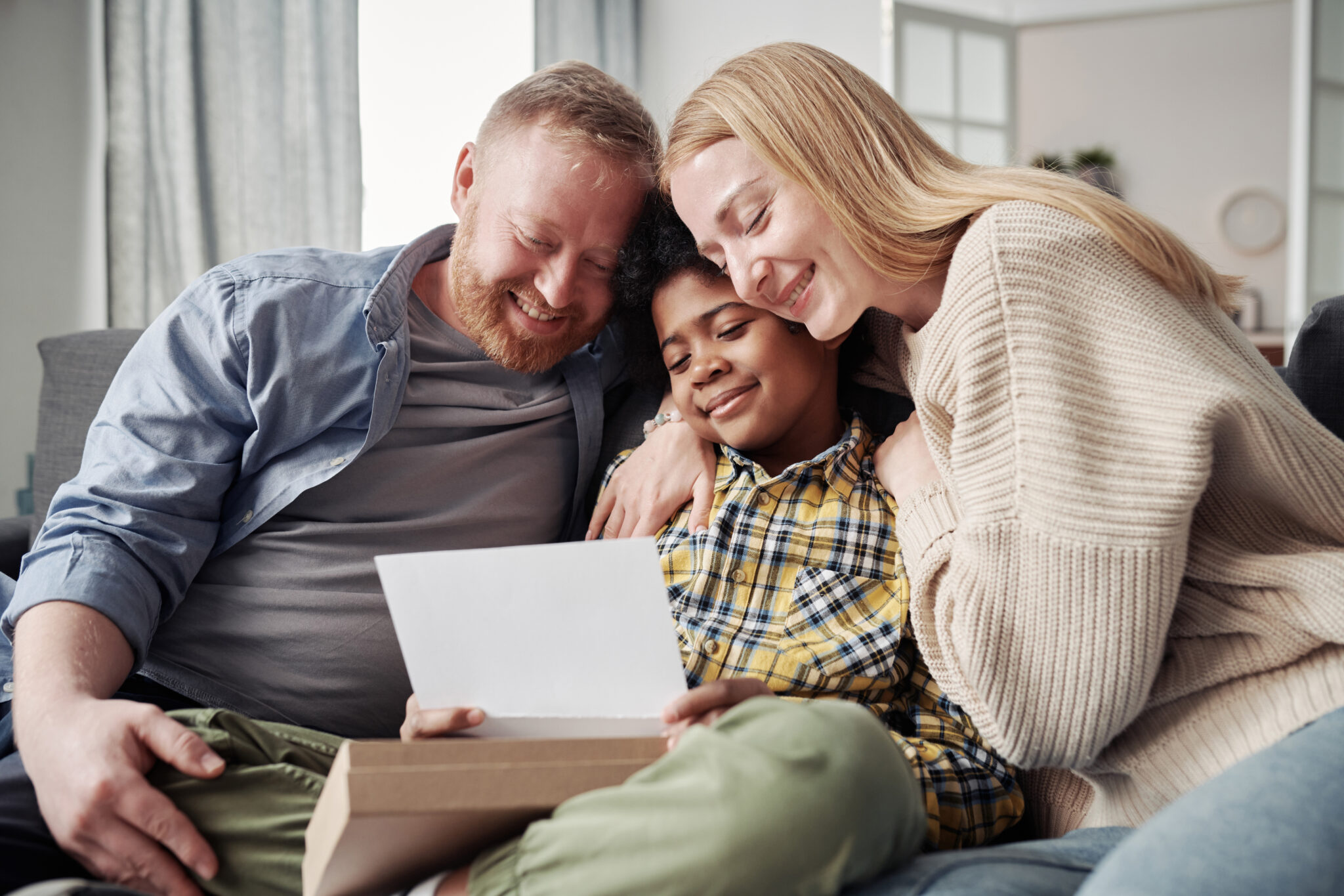 Happy parents embracing their African adoptive son while reading adoption agreement together on sofa